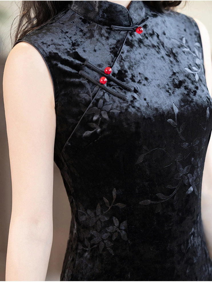 Close-up of a sleeveless black velvet cheongsam-style top with tonal floral embroidery and red decorative buttons, worn by a model.