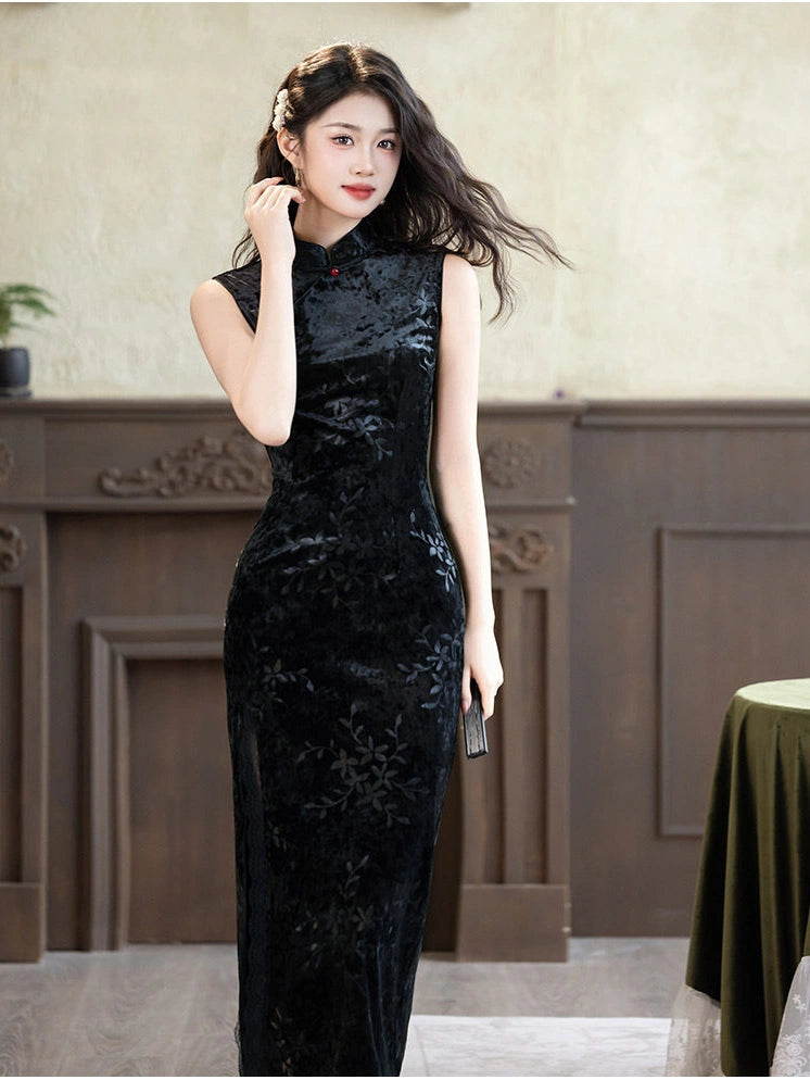 A woman wearing a sleeveless black velvet cheongsam dress with tonal floral embroidery, standing in an indoor setting with a brown wooden panel wall.