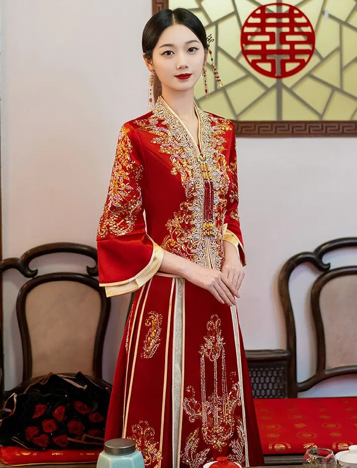 Woman in a traditional red and gold Modernized V-Neck Chinese Wedding Xiu He Qun Kwa Dress with intricate patterns, standing in a room with decorative elements.