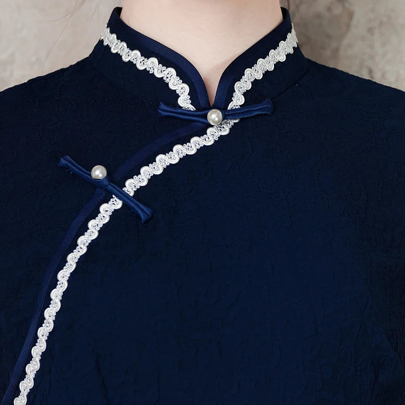 Navy blue traditional  chinese cheongsam outfit with white lace trim and pearl buttons on a neutral background