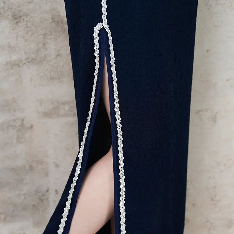 Navy blue dress with a high slit and decorative trim on a neutral background