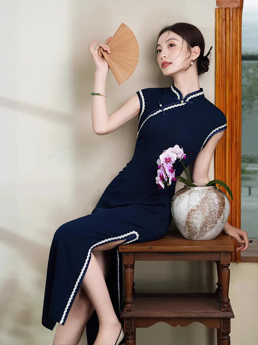 Woman in a Navy Blue Cap Sleeves Jacquard Cotton Qipao Dress  traditional chinese dress holding a wooden fan and a pink orchid, sitting on a wooden chair.