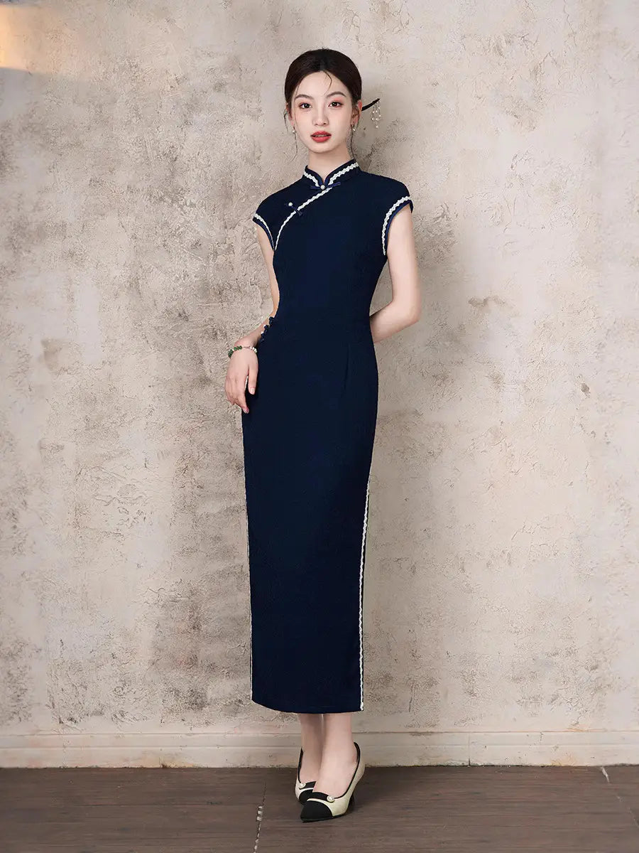 Woman wearing a  Navy Blue Cap Sleeves Jacquard Cotton chinese cheongsam Dress with white trim against a textured wall.