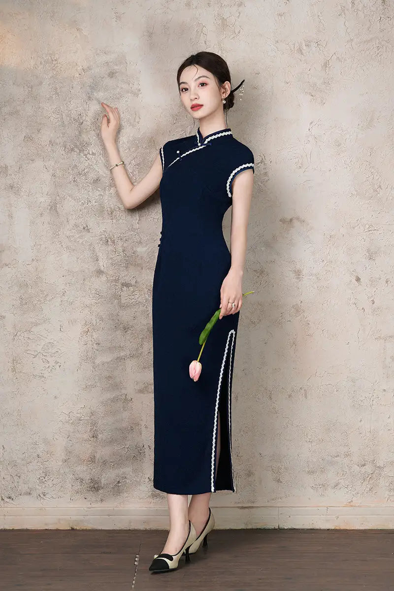 Woman in a Navy Blue Cap Sleeves Jacquard Cotton Qipao Dress  holding a pink flower against a textured wall.