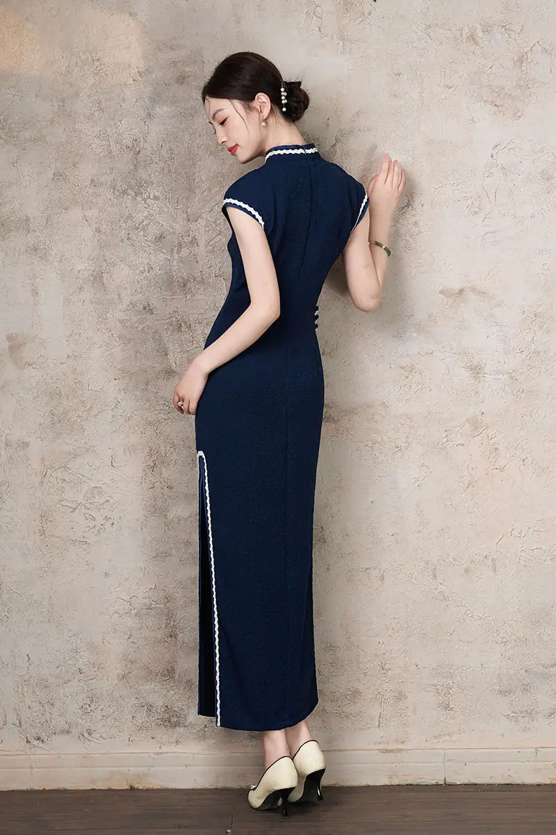 Woman wearing a Navy Blue Cap Sleeves Jacquard Cotton Qipao Dress with white trim against a textured wall.