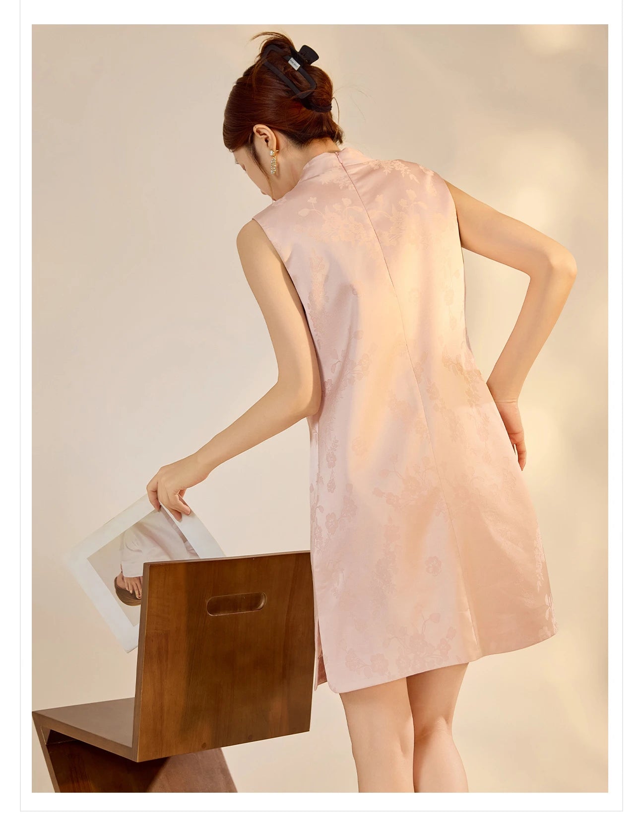 Woman wearing a light pink qipao sleeveless dress holding a wooden stool.