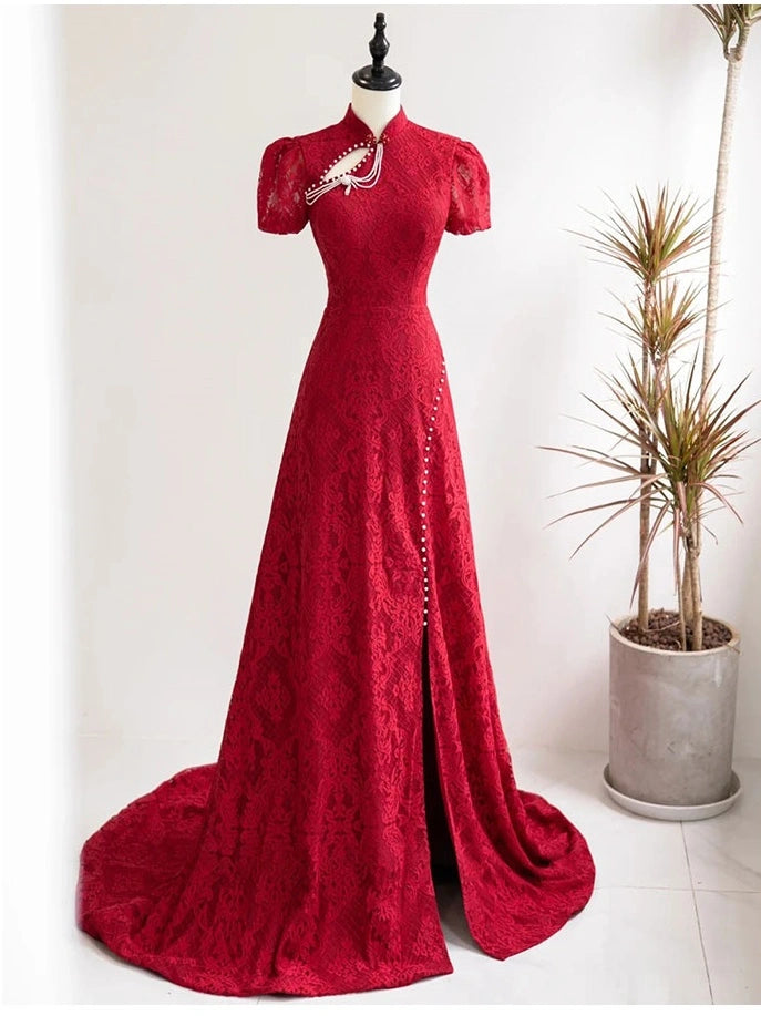 A floor-length red Open Back Lace Cheongsam/Qipao Dress With Train  formal gown displayed on a black mannequin in a bright indoor setting. The dress has short puff sleeves, a high mock neck, decorative silver embellishments along the neckline and side slit, and a slight train.