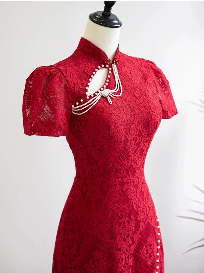A red lace cheongsam-style dress displayed on a mannequin torso against a light neutral background. The dress features short puff sleeves, a high collar, and a decorative neckline with white pearl-like strands and a bow detail.