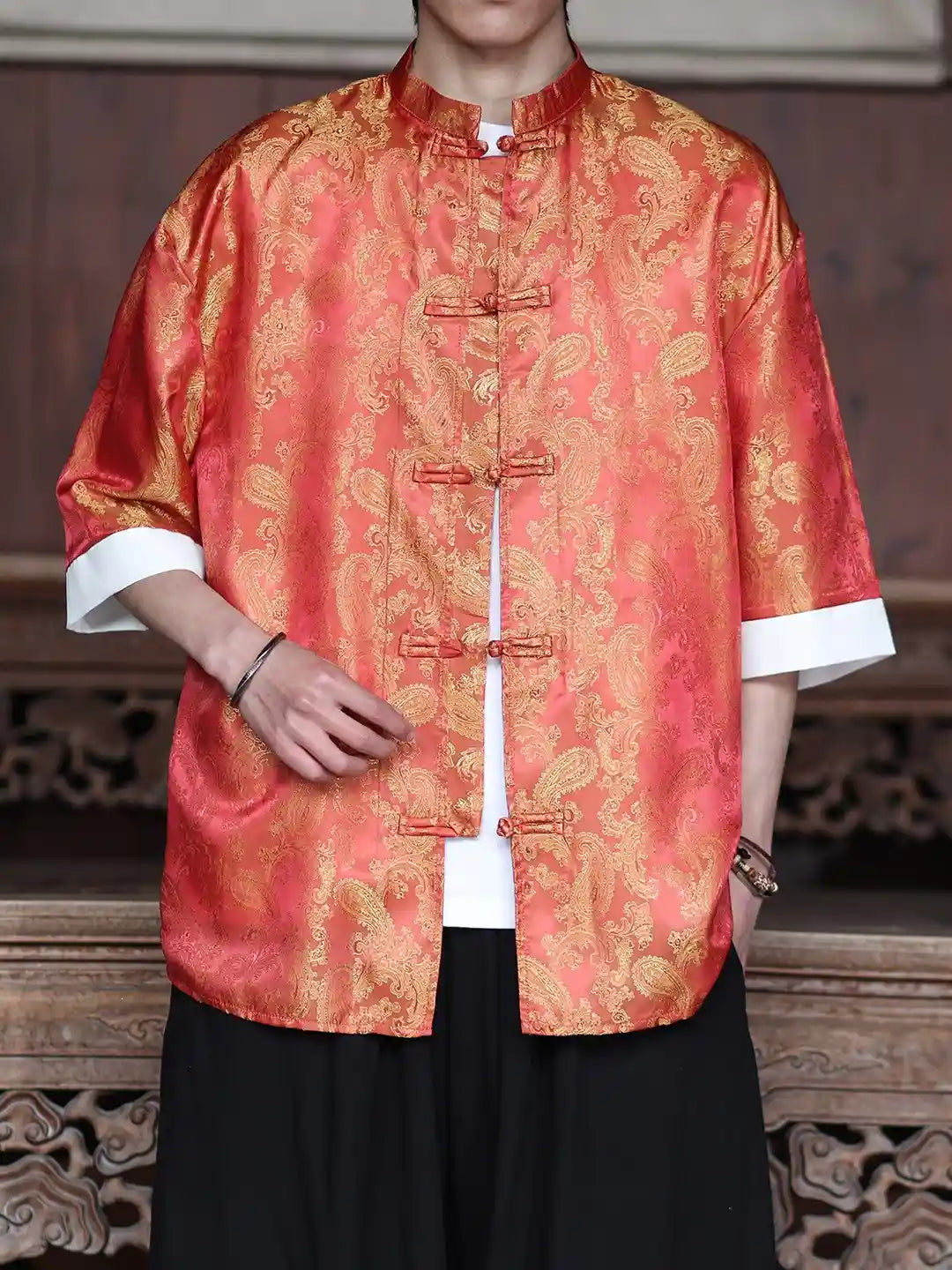 Person wearing a traditional orange  and gold patterned Modern New Chinese Style Men's Half Sleeve Jacquard Tang Shirt with white cuffs and black pants.