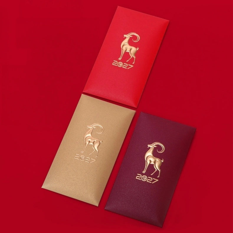 Three textured red envelopes arranged diagonally on a solid red background. Each envelope features a metallic gold foil illustration of a ram/goat/sheep and the year '2027'.