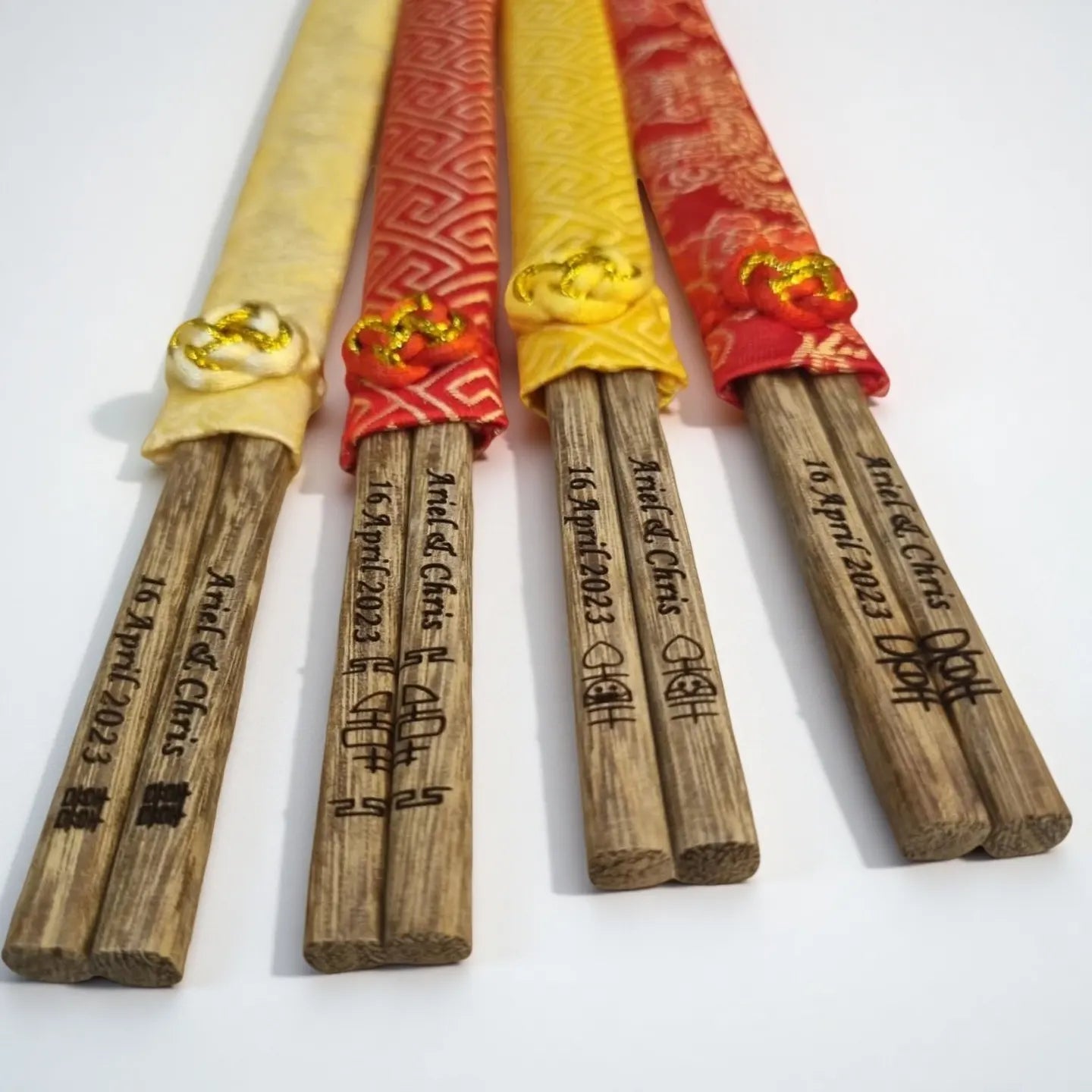Four wooden chopsticks with brocade  sleeves  and engraved text on a white background