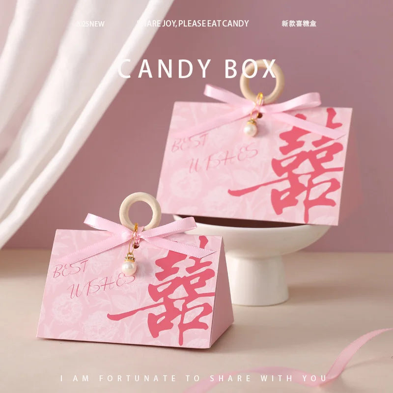 Two pink Floral Triangular Shape Double Happiness Favor Boxes candy boxes with ribbons and charms on a light pink background 