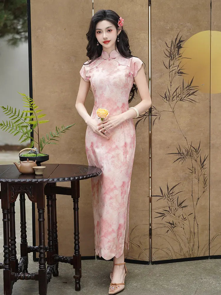 Woman in a chinese Pink Floral Watercolor Long Qipao Dress  standing in front of a decorative screen with plants on a table.