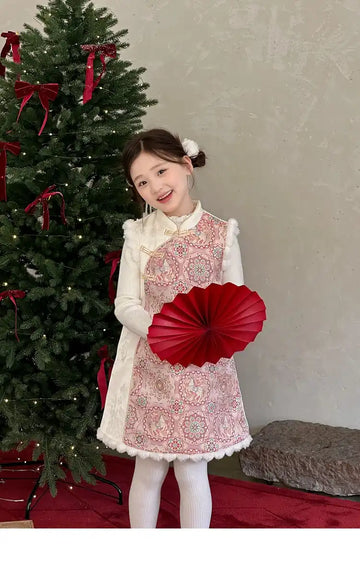 Young girl in a Pink Quilted  Girls’ Winter Qipao Vest  setting with a decorated Christmas tree, holding a red fan.