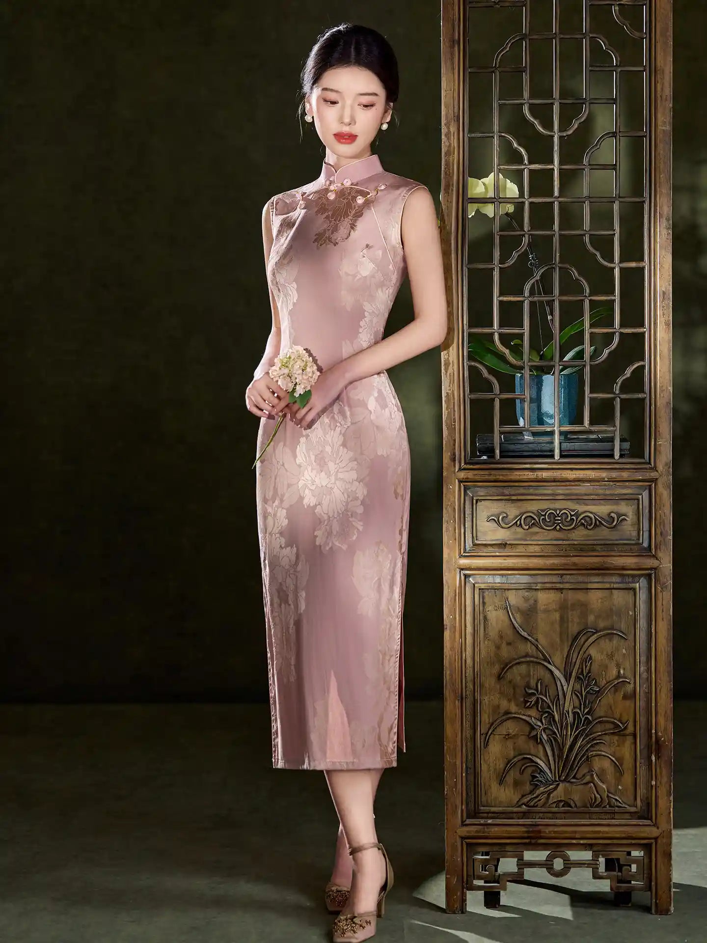 Woman in a Pink Sleeveless Floral Jacquard Satin Qipao Dress  standing in front of a wooden cabinet.