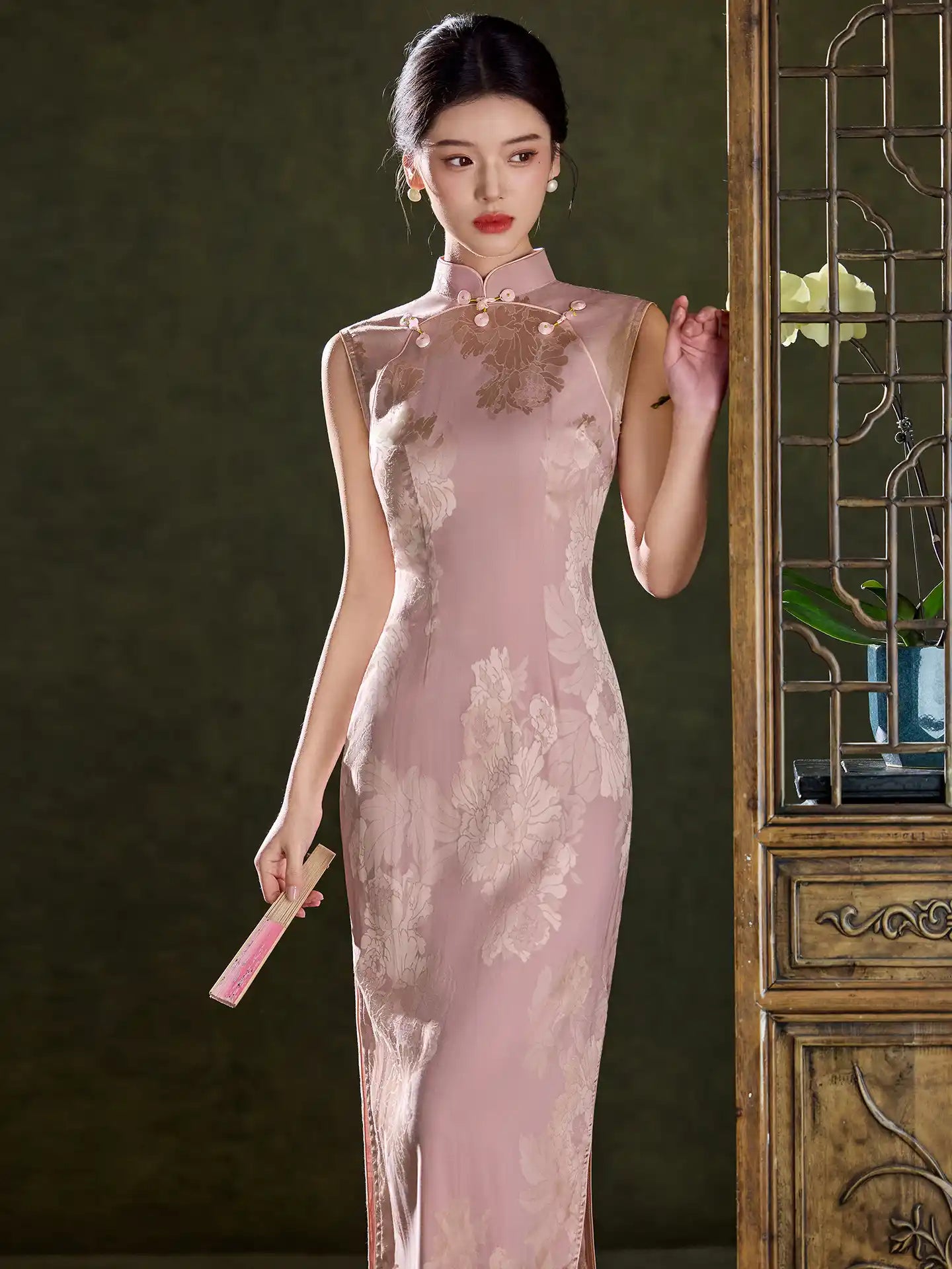 Woman in a Pink Sleeveless Floral Jacquard Satin Qipao Dress  standing next to a decorative screen.