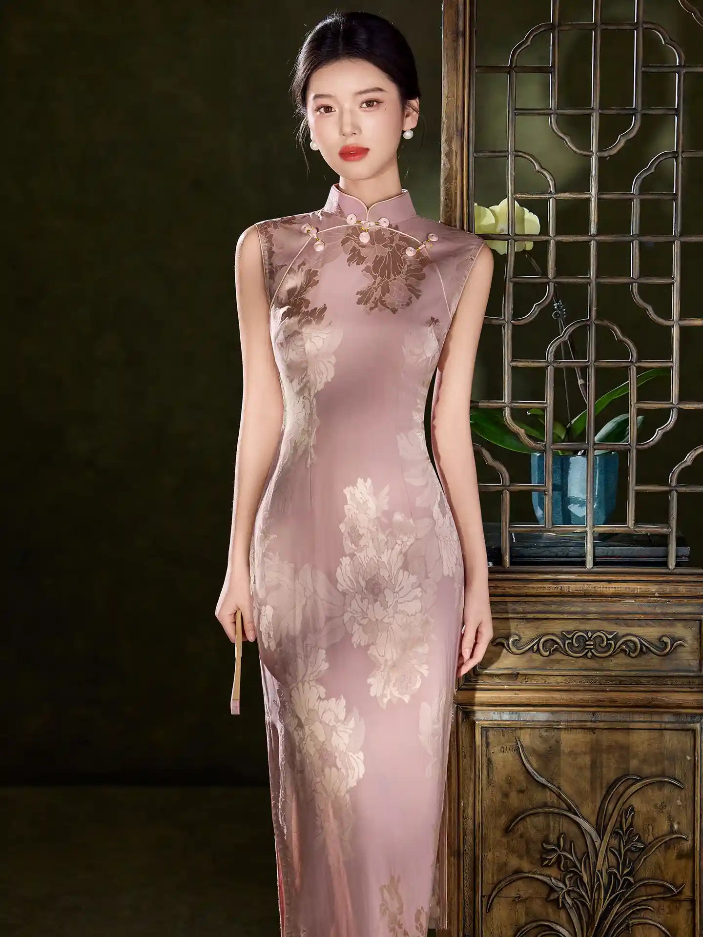 Woman wearing aPink Sleeveless Floral Jacquard Satin Qipao Dress  in a dark room with decorative elements