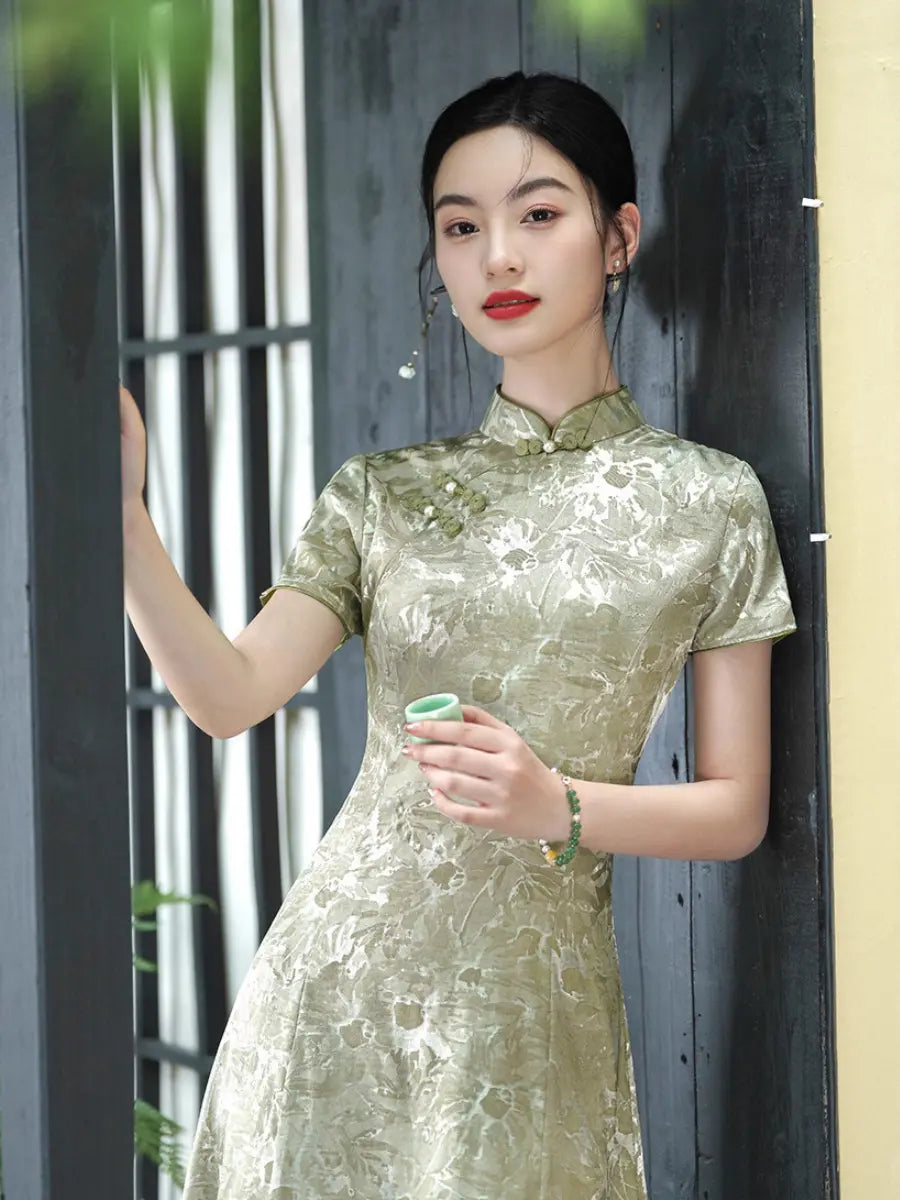 A woman wearing a short-sleeved Pistachio Sage Green Floral Jacquard Modern A Line Qipao  cheongsam dress with a tonal floral pattern, holding a small green cup in front of a dark wooden door.