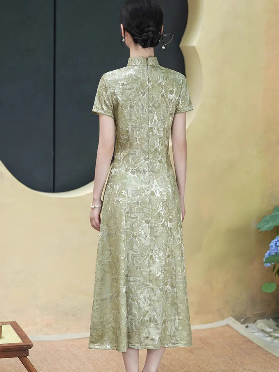 A woman viewed from behind wearing a short-sleeved, Pistachio Sage Green Floral Jacquard Modern A Line Qipao midi dress with a textured, metallic gold-green floral pattern. The dress features a shawl collar and a structured waist.