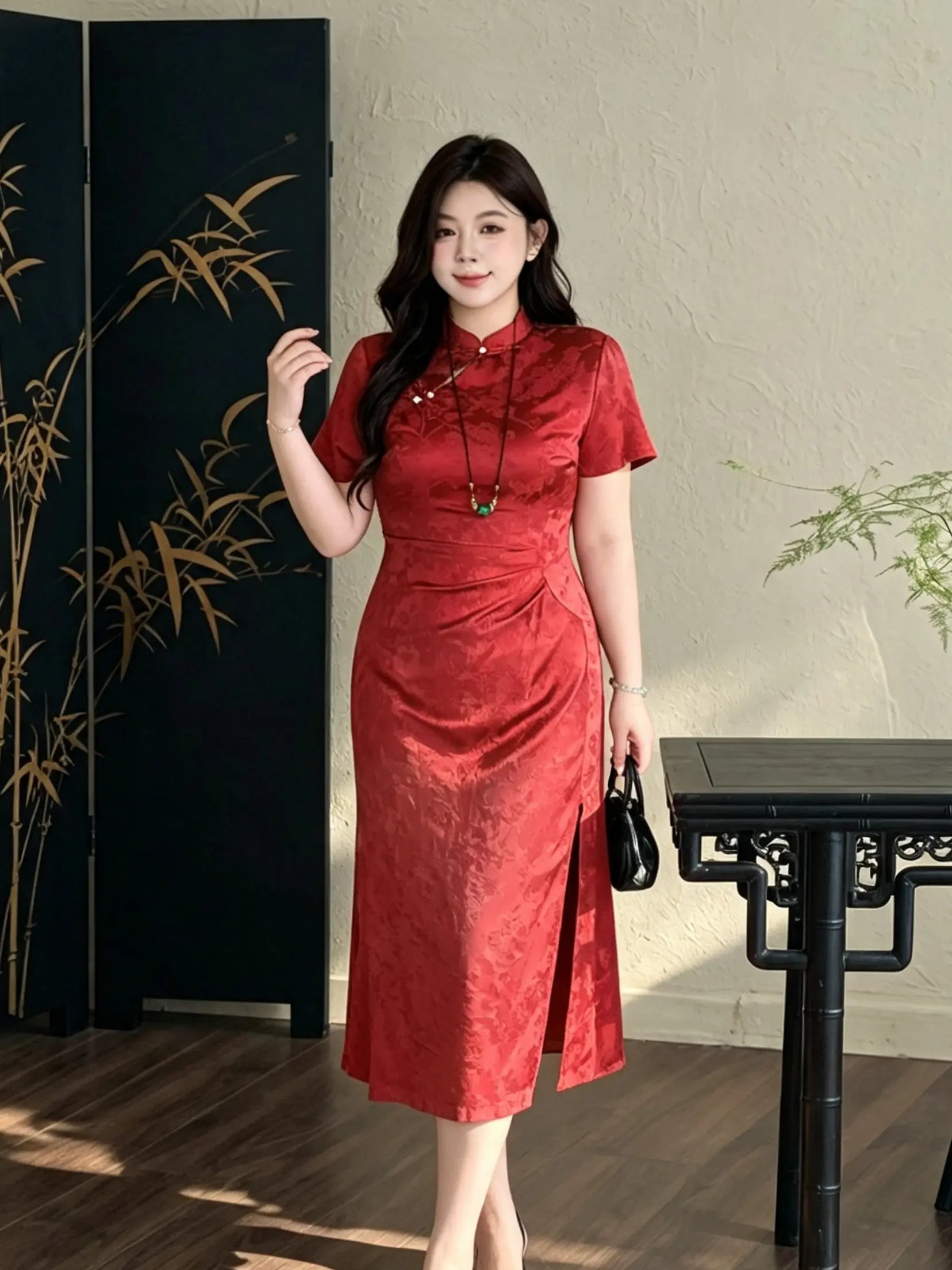 A woman modeling a  short-sleeve Plus Size Cinnabar Red Modern midi  Qipao  cheongsam dress with a textured jacquard pattern, standing in a styled indoor setting with a black folding screen and wooden table.