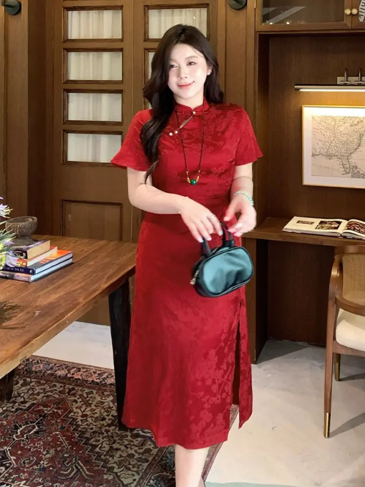 A woman wearing a Plus Size Cinnabar Red Modern midi  Qipao  cheongsam dress with a subtle tonal floral pattern, standing in a warm wood-paneled room and holding a small dark green handbag.
