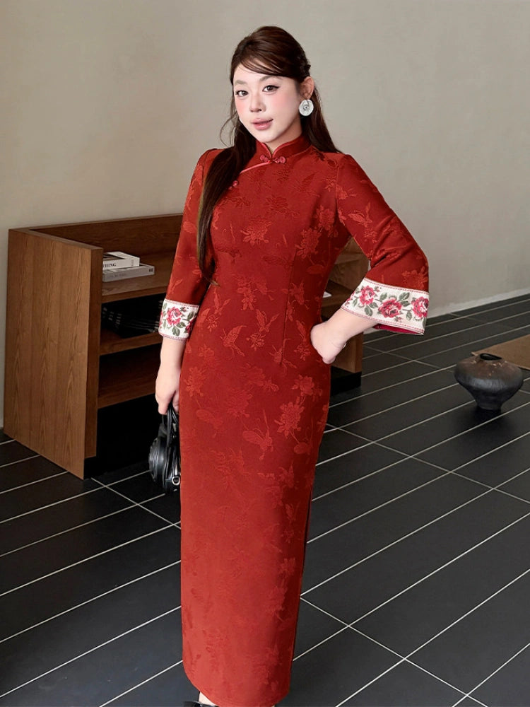 A woman wearing a Plus Size Crimson Red Floral Jacquard Long Sleeve Qipao cheongsam dress with floral embroidery on the cuffs, standing in an indoor setting with a tiled floor.