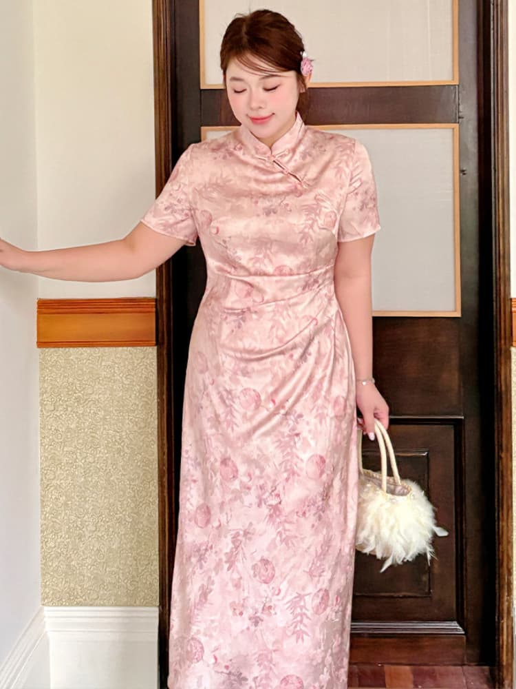 A woman wearing a light pink satin plus size qipao cheongsam dress with a floral pattern, holding a white fluffy handbag, standing in front of a dark wooden door.
