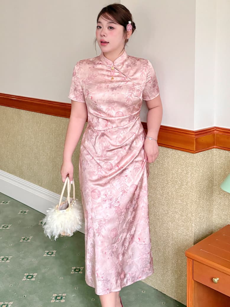 A woman wearing a pink floral satin plus size cheongsam dress, holding a white feathered handbag in an indoor setting with a beige wall and green patterned carpet.