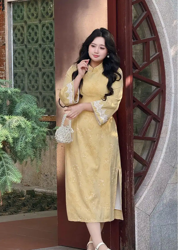 Woman in a Plus Size Golden Yellow Long Sleeve Jacquard Qipao dress with Lace Trim  standing in front of a decorative door.