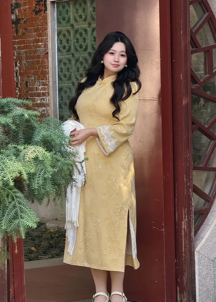 Woman in a Plus Size Golden Yellow Long Sleeve Jacquard cheongsam Qipao with Lace Trim standing in front of a traditional door with decorative patterns.