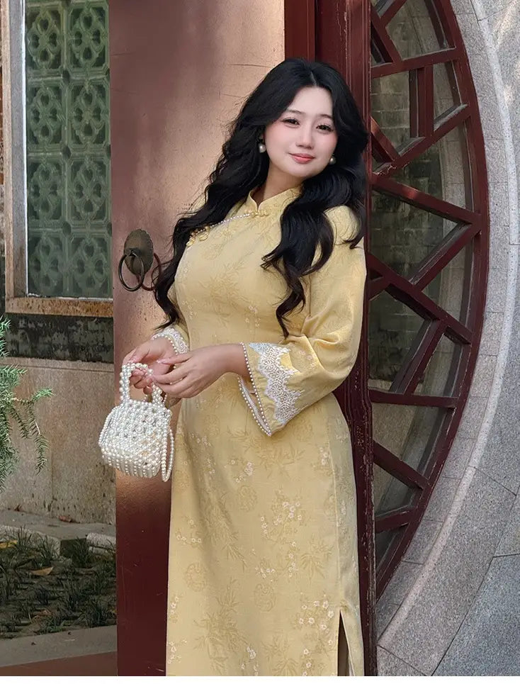 Woman in a Plus Size Golden Yellow Long Sleeve Jacquard Qipao cheongsam with Lace Trim holding a white handbag in front of a decorative door.