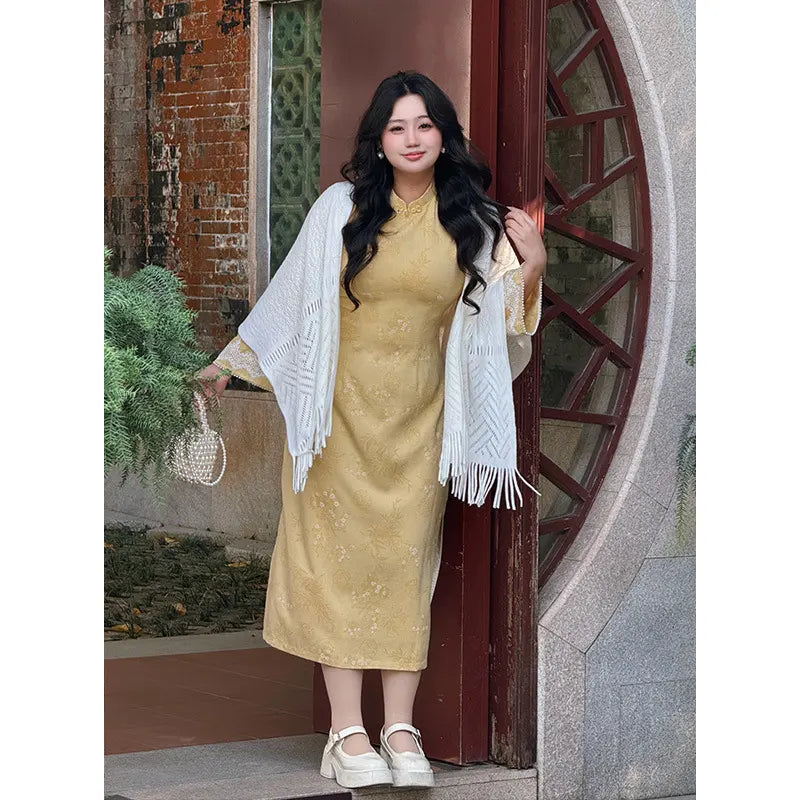 Woman in a Plus Size Golden Yellow Long Sleeve Jacquard Qipao with Lace Trim with a white shawl standing in front of a round stone archway.