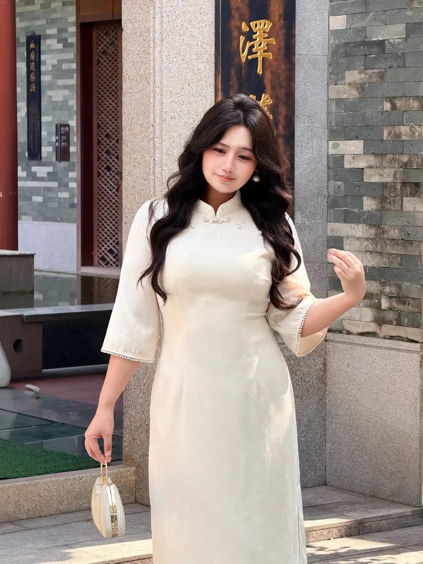 Woman in a Plus Size Ivory White Floral Long Sleeve Jacquard Qipao cheongsam standing in front of a stone wall with Chinese characters.