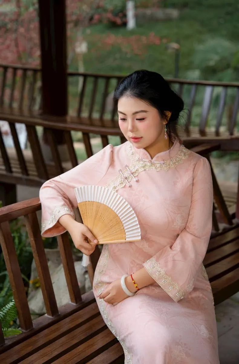 Woman in A  traditional  Plus Size Long Sleeve Pink Floral Qipao with Pearl Trim dress holding a fan on a wooden deck.