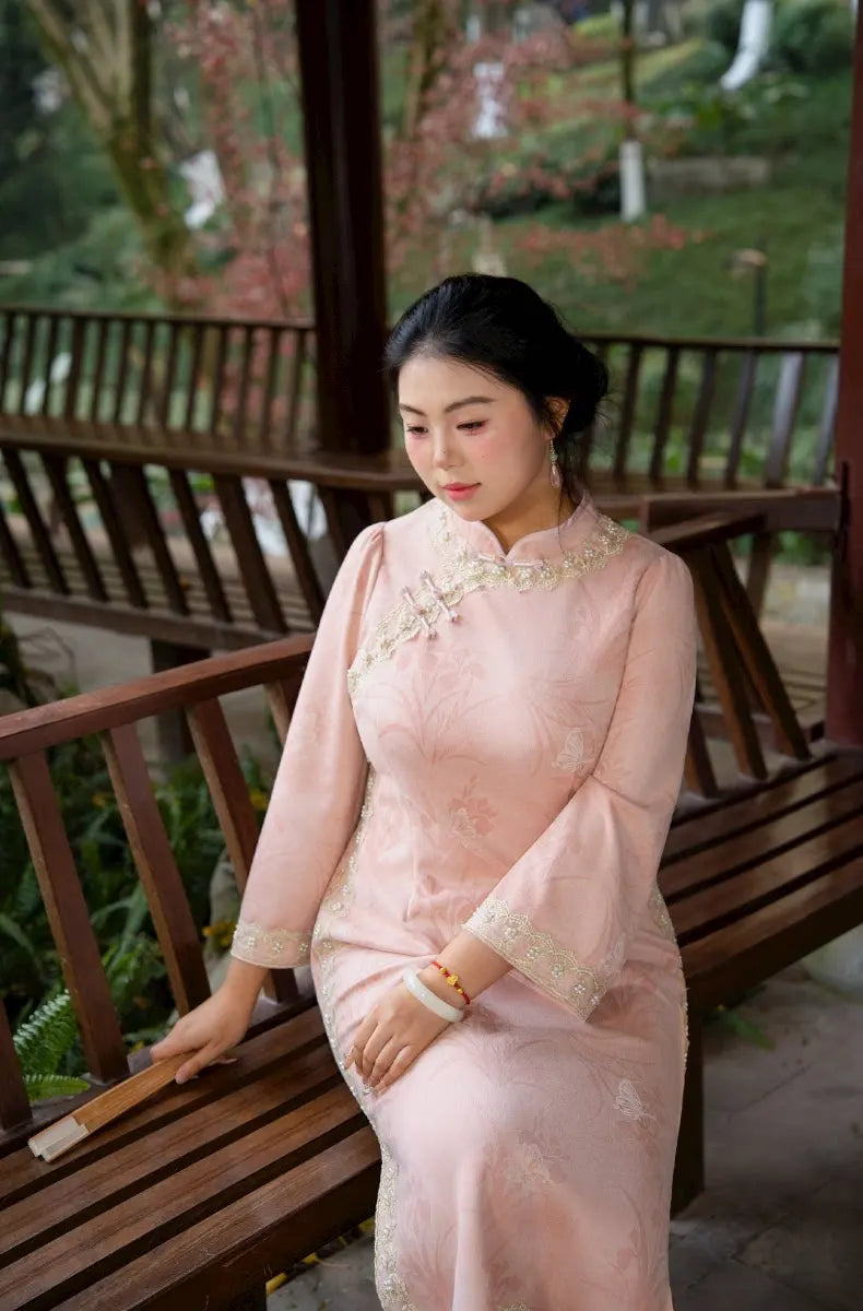 Woman in a traditional Plus Size Long Sleeve Pink Floral Qipao Cheongsam with Pearl Trim dress sitting on a wooden bench outdoors.