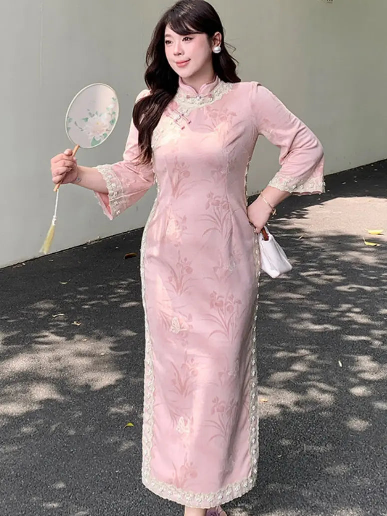 A woman wearing a light pink traditional Chinese long sleeve cheongsam dress with floral embroidery and lace trim, holding a decorative fan outdoors.