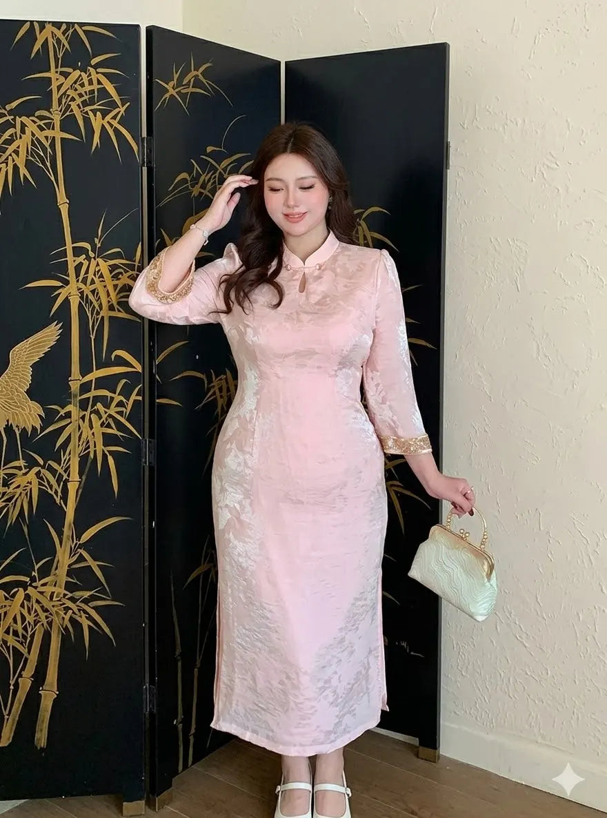 Woman in a Plus Size Modern Pink Long Sleeve Jacquard Qipao dress standing in front of a black screen with gold bamboo design.
