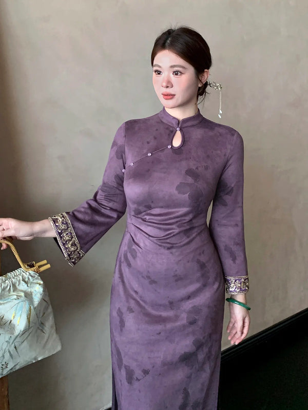 A woman wearing a purple long-sleeve plus size cheongsam dress with a keyhole neckline and ornate patterned cuffs, holding a light-colored handbag against a neutral indoor background.