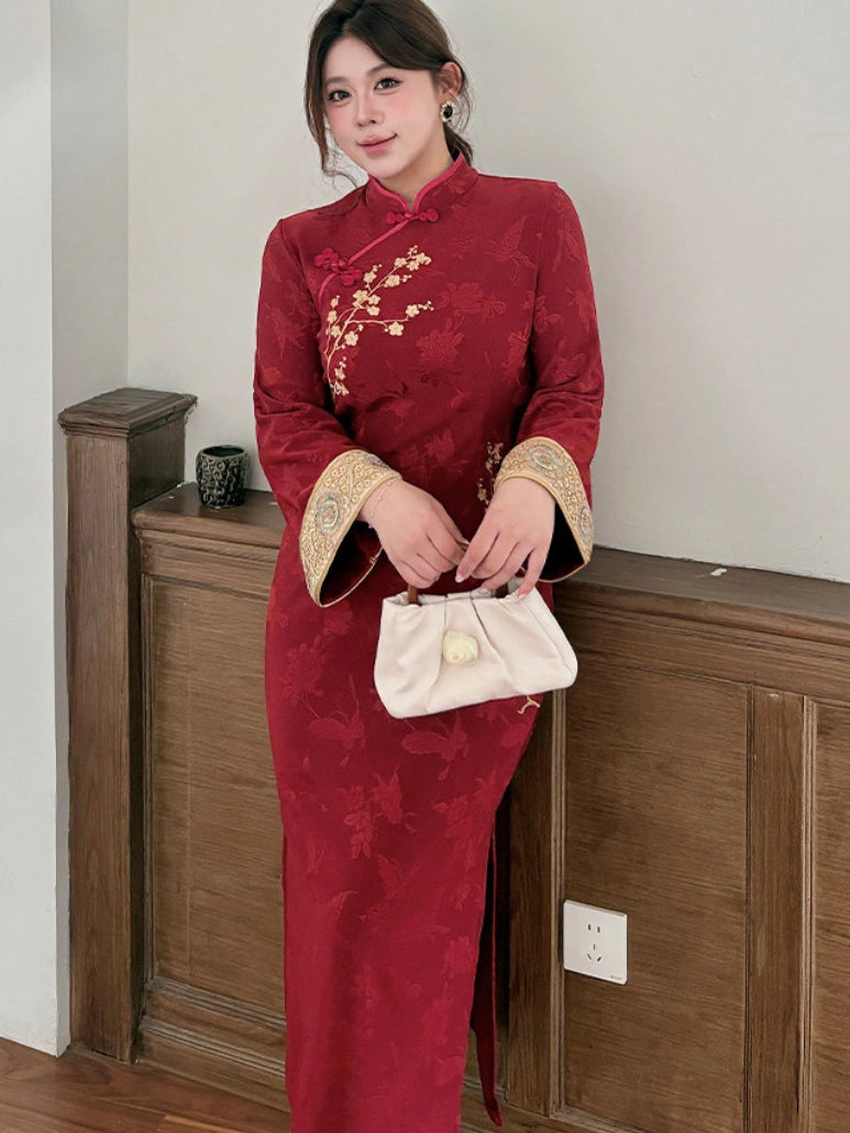 A woman wearing a traditional Chinese cheongsam (qipao) dress in deep red with gold floral embroidery and gold-trimmed cuffs, holding a cream-colored clutch purse.