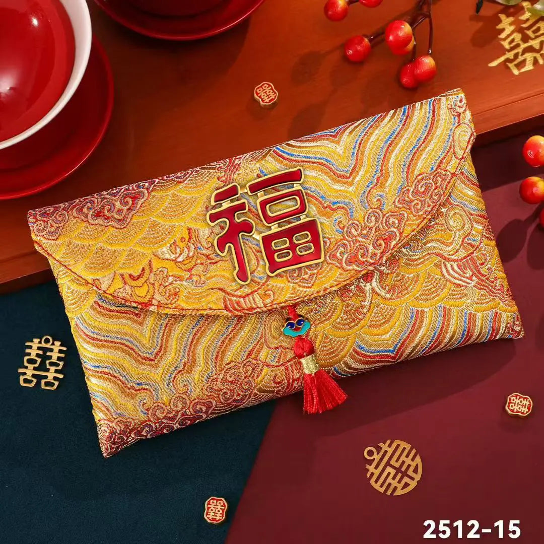 A red and gold Chinese New Year envelope clutch bag with a dragon and cloud brocade pattern, featuring a red Chinese character 'Fu' on the front flap and a red tassel with a blue bead. The clutch is displayed on a dark wooden table decorated with red teacups, red berries, gold double happiness charms, and a dark red envelope underneath.