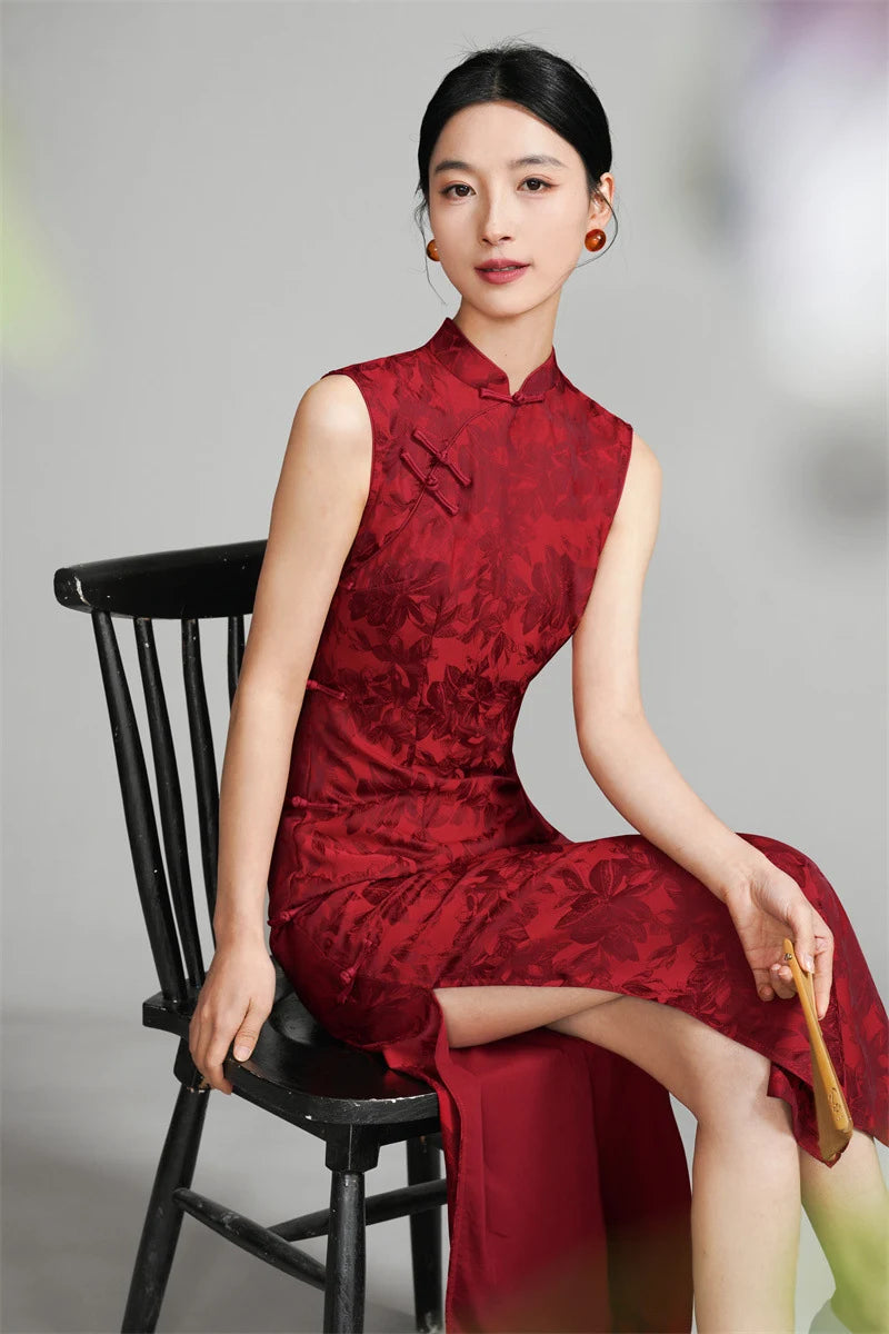 a Chinese woman in a red wedding cheongsam sitting on a black chair against a gray background