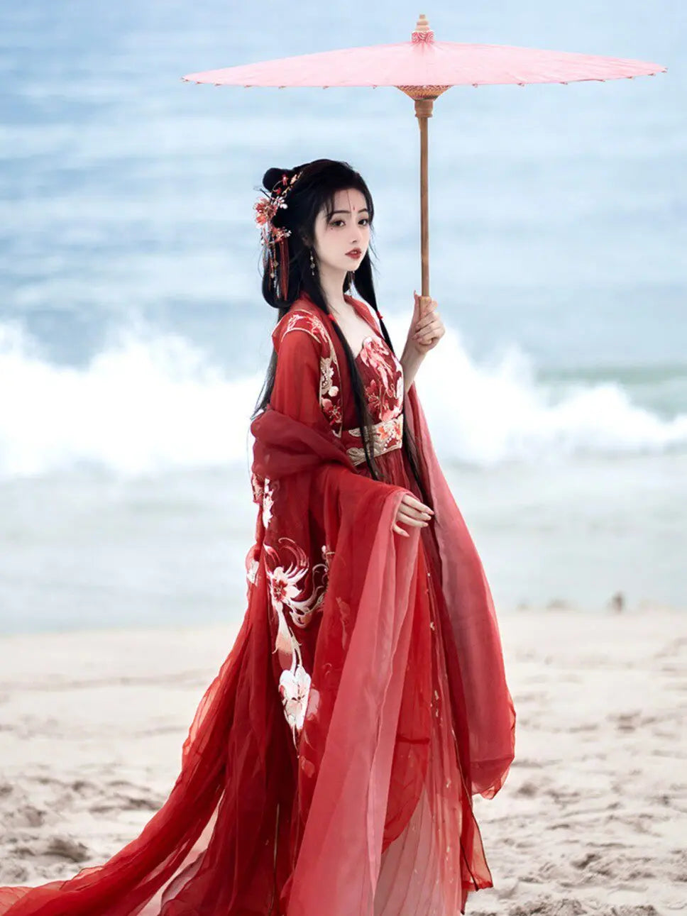 Woman in traditional Red Ancient Chinese Imperial Tang Dynasty Hanfu Set holding a pink parasol on a beach