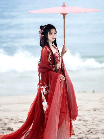 Woman in traditional Red Ancient Chinese Imperial Tang Dynasty Hanfu Set holding a pink parasol on a beach