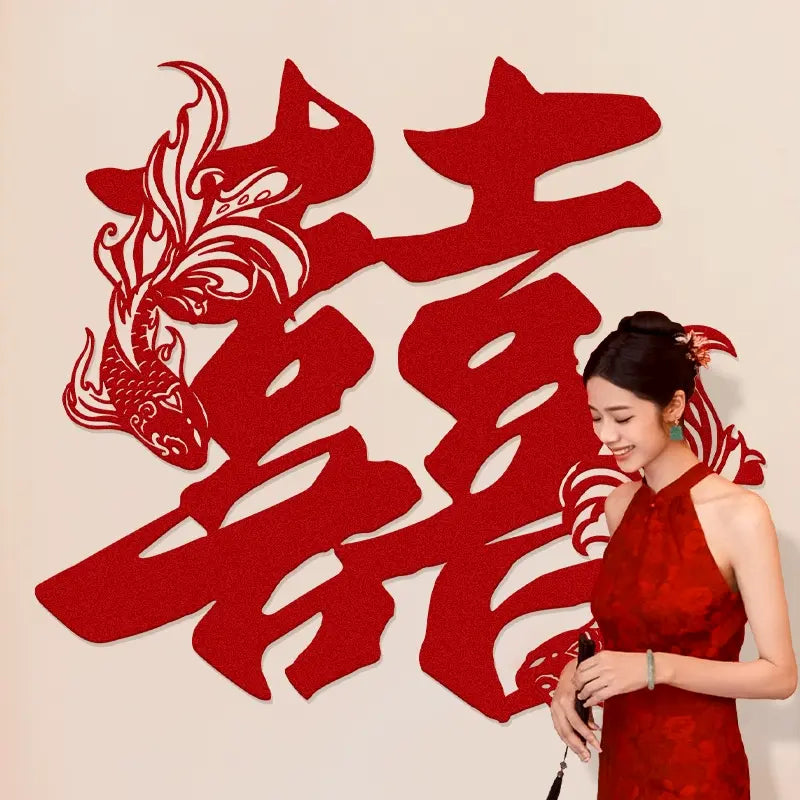 Woman in a red dress standing next to large red Chinese double happiness wedding back drop with a fish design on a beige background
