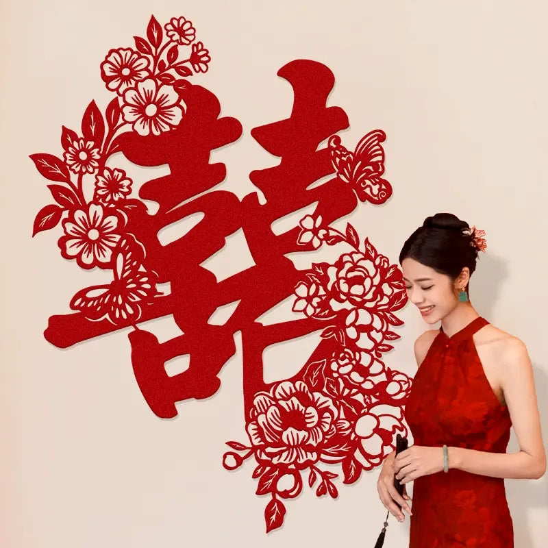 Woman in a red dress standing next to a large red decorative chinese wedding double happiness backdrop decor with floral elements on a beige background
