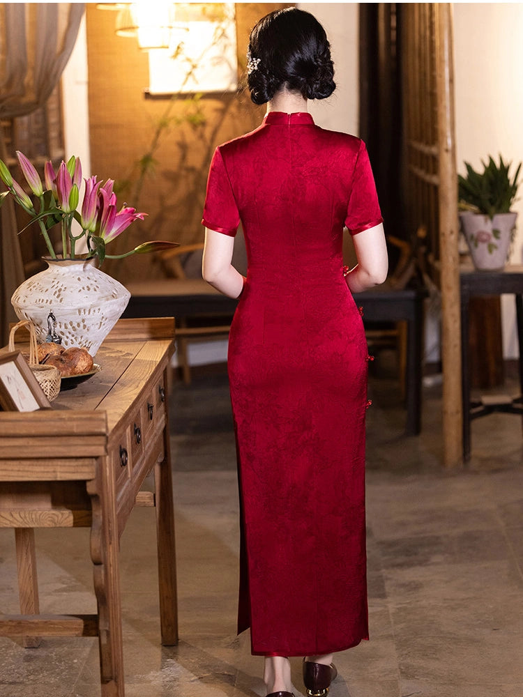 A woman viewed from behind wearing a long, red, short-sleeved cheongsam/qipao dress in a traditional Chinese-style room with wooden furniture and warm lighting.