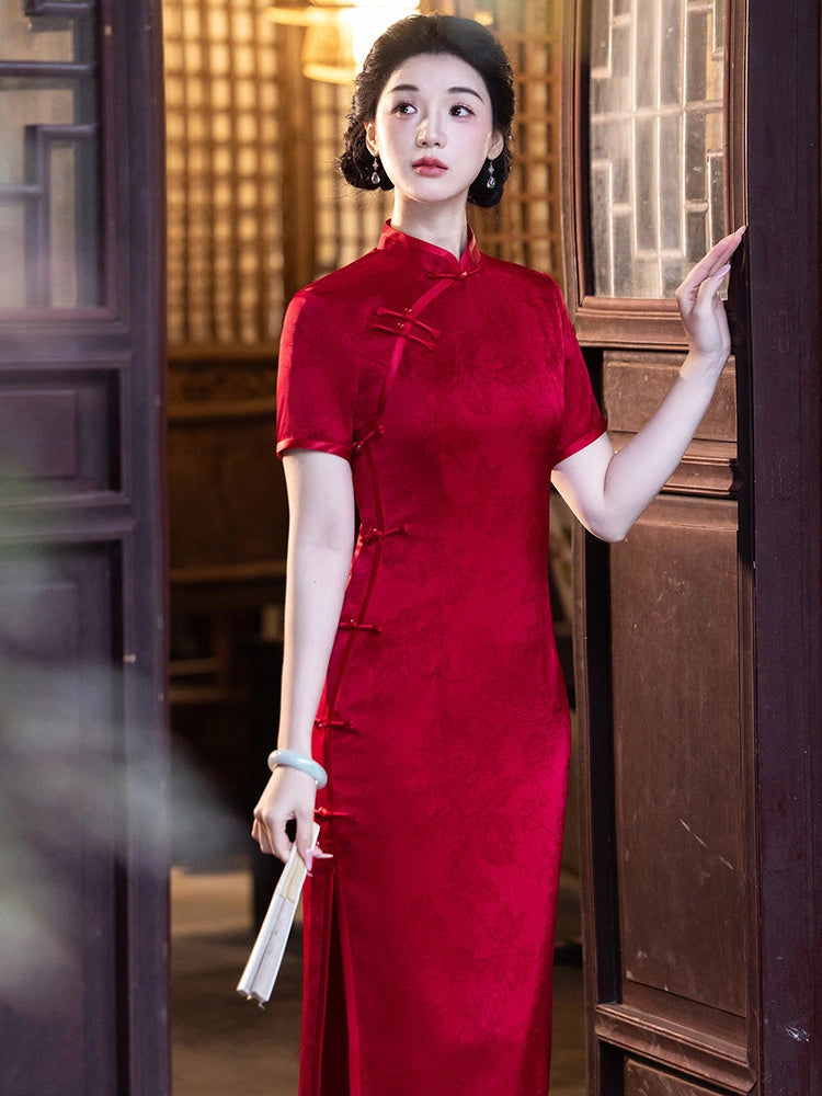 A woman wearing a traditional red Chinese cheongsam dress with short sleeves and a high collar, standing in a doorway with wooden paneling.