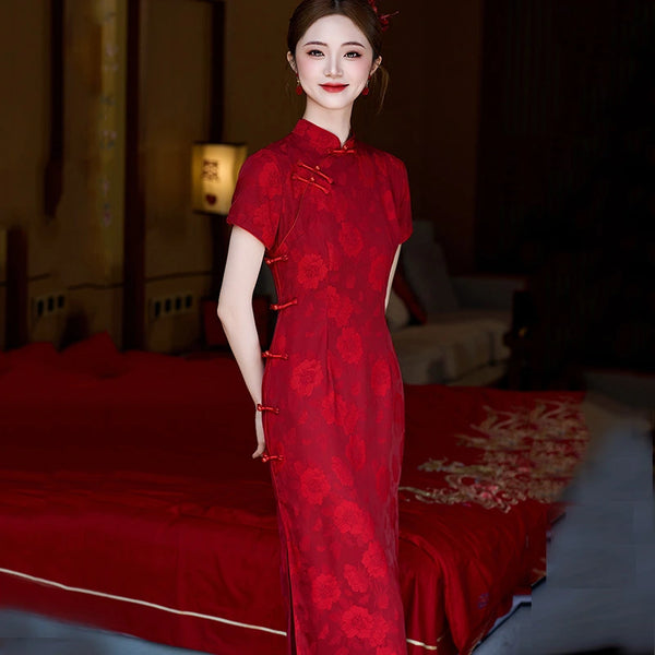 Woman in a red traditional  Floral Qipao Cheongsam Dress standing in a room with a bed and lamp.