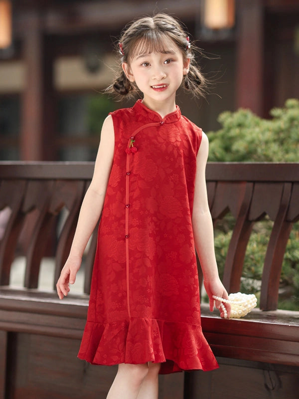 A young girl with braided hair wearing a sleeveless red Chinese cheongsam-style dress with a ruffled hem, standing outdoors in front of a wooden railing.