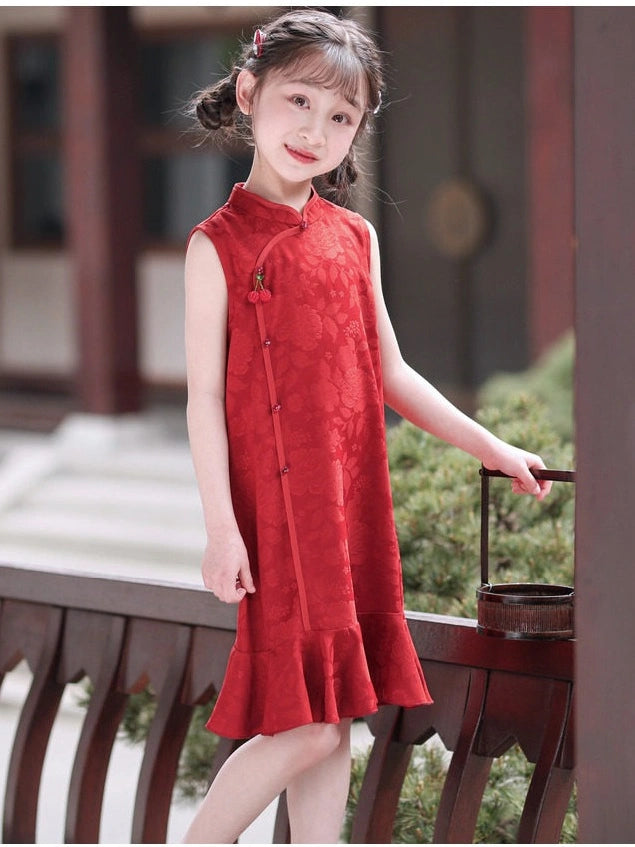 A young girl wearing a sleeveless red Chinese cheongsam dress with a ruffled hem, standing in a traditional courtyard next to a wooden railing.